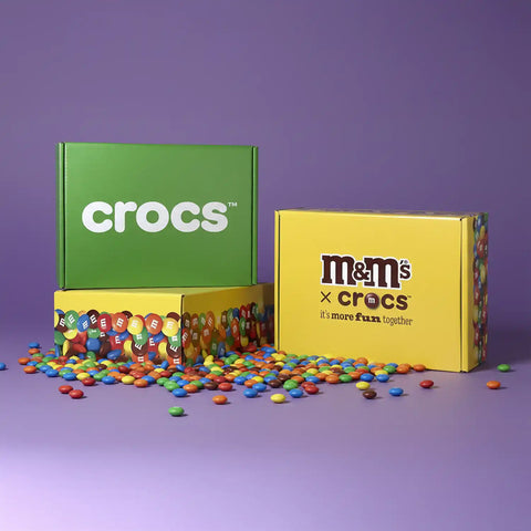 Image of Crocs and M&M's boxes with colorful candies on a purple background