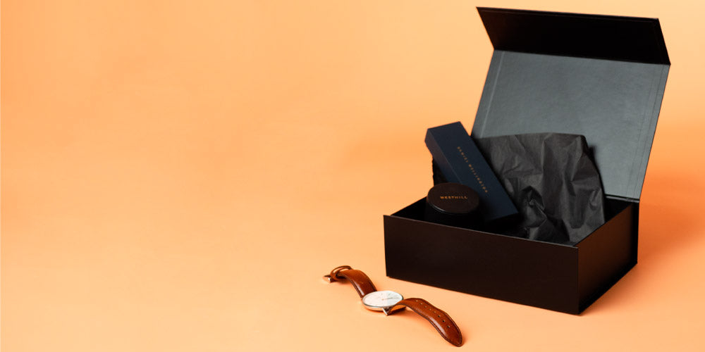Premium Magnetic Gift Box Black with Black Tissue Paper featured on a Peach Background and a Men's Dress Watch as a prop. Elegant Magnetic Gift Boxes. Available in low minimum order quantities unbranded or Custom Printed with your Logo or Brand